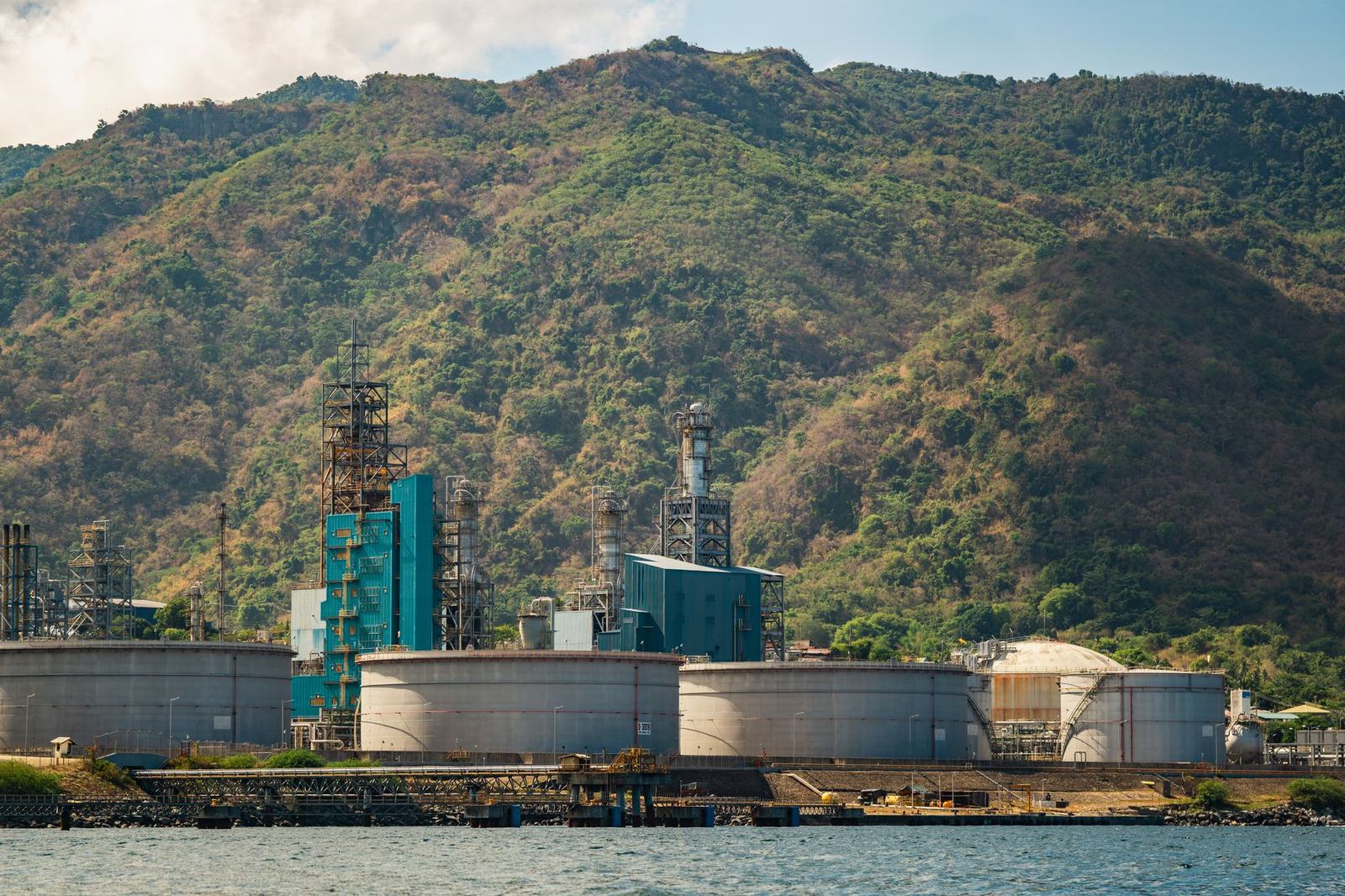 Παράκτια βιομηχανική μονάδα με μεγάλες δεξαμενές κάτω από πράσινους λόφους