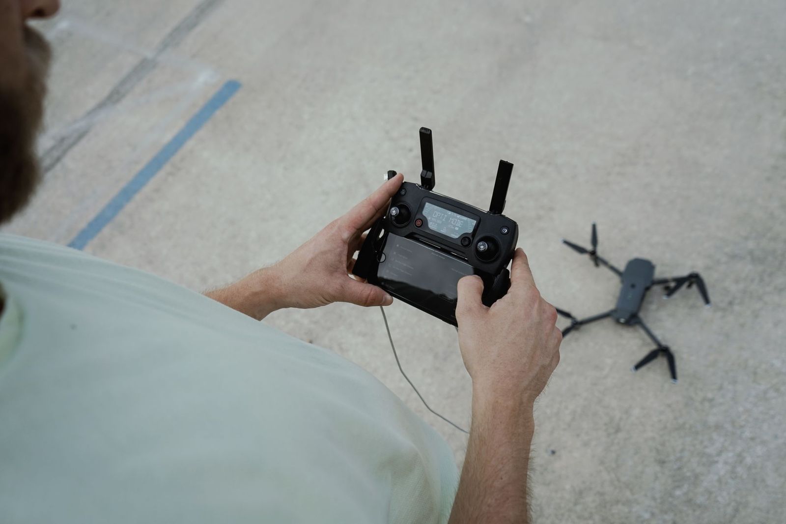 Χειριστής κρατά το χειριστήριο drone, με το drone ακουμπισμένο στο σκυρόδεμα δίπλα του