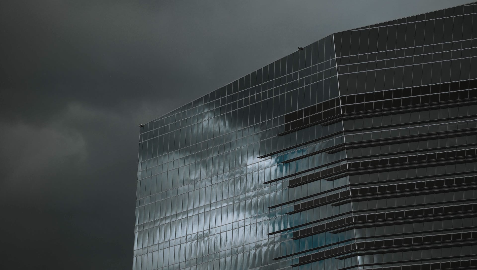 Glass façade of a high-rise building under a dark, overcast sky